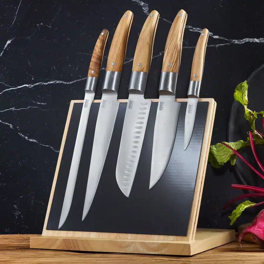 Magnetischer Messerblock mit fünf Küchenmessern und Olivenholzgriffen auf schwarzem Marmor.