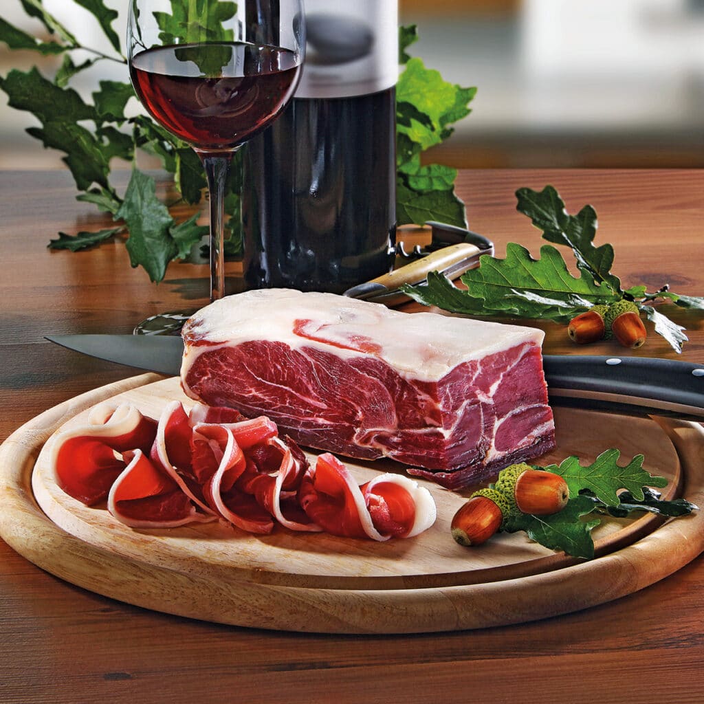 Scheibe roh geräuchertes Fleisch auf Holzbrett mit geschnittenem Schinken und Rotweinglas.