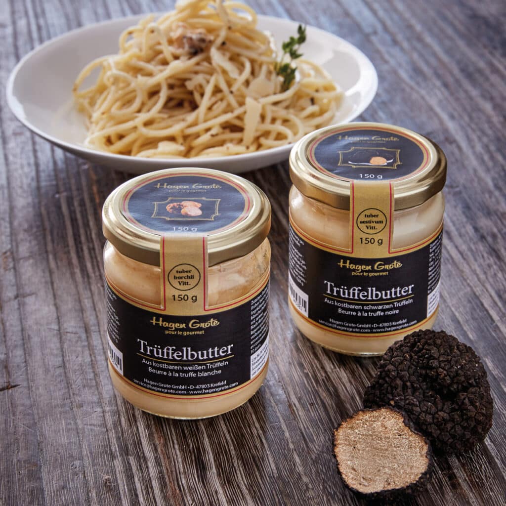 Zwei Gläser Trüffelbutter von Hagen Grote vor einem Teller Pasta und frischer schwarzer Trüffel.