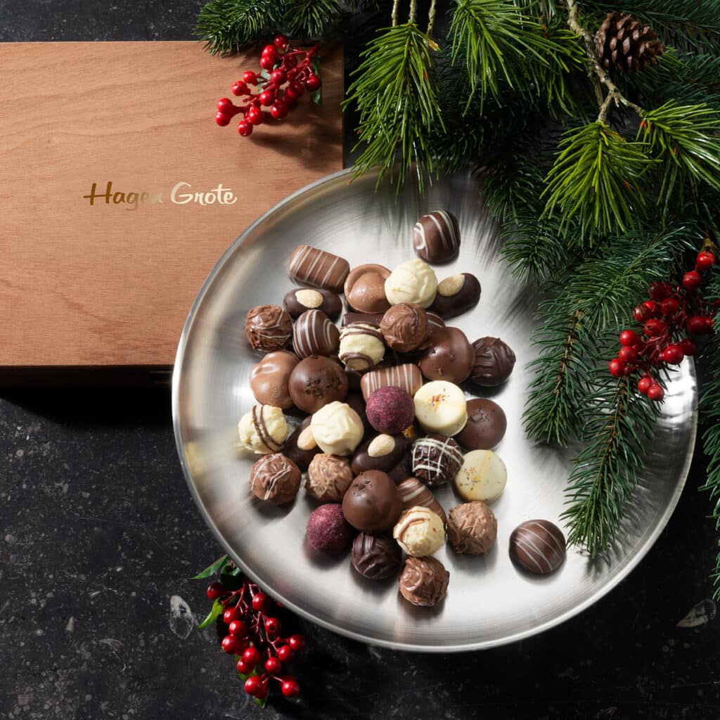 Edle Pralinenmischung auf Silberplatte mit hölzerner Hagen Grote Box und Tannenzweigen.