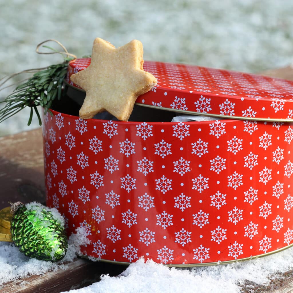 Rote Keksdose mit Schneeflocken-Muster, dekoriert mit Stern-Plätzchen im Schnee