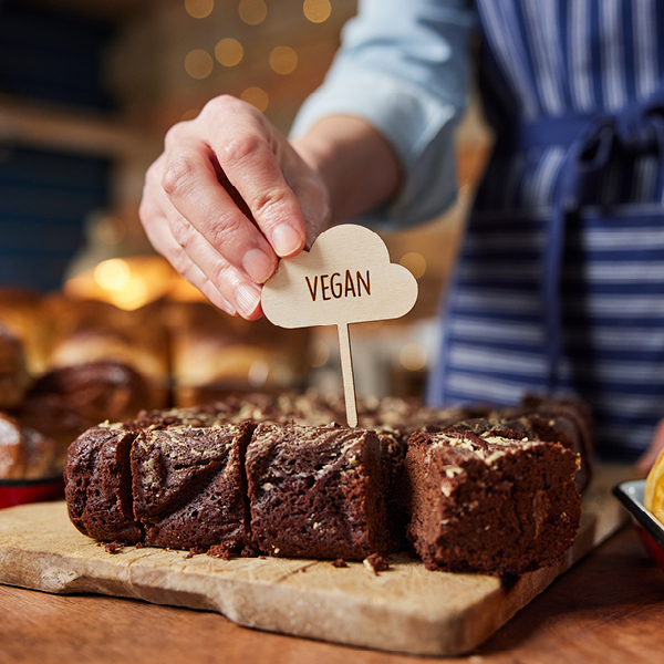 Kuchen auf einem Brett und eine Person steckt ein Schild mit der Aufschrift "vegan" in den Kuchen