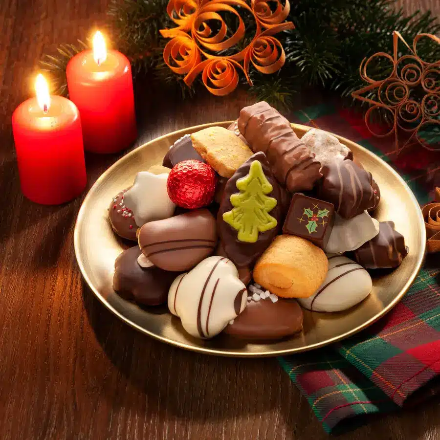 Adventsgebäck auf goldenem Teller – weihnachtliche Plätzchen mit Schokolade, Marzipan und Zuckerdekor neben roten Kerzen