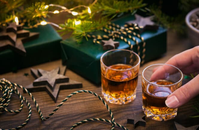 Zwei Gläser Weihnachtslikör auf Holztisch mit Tannenzweig, Stern-Deko und Geschenkverpackung