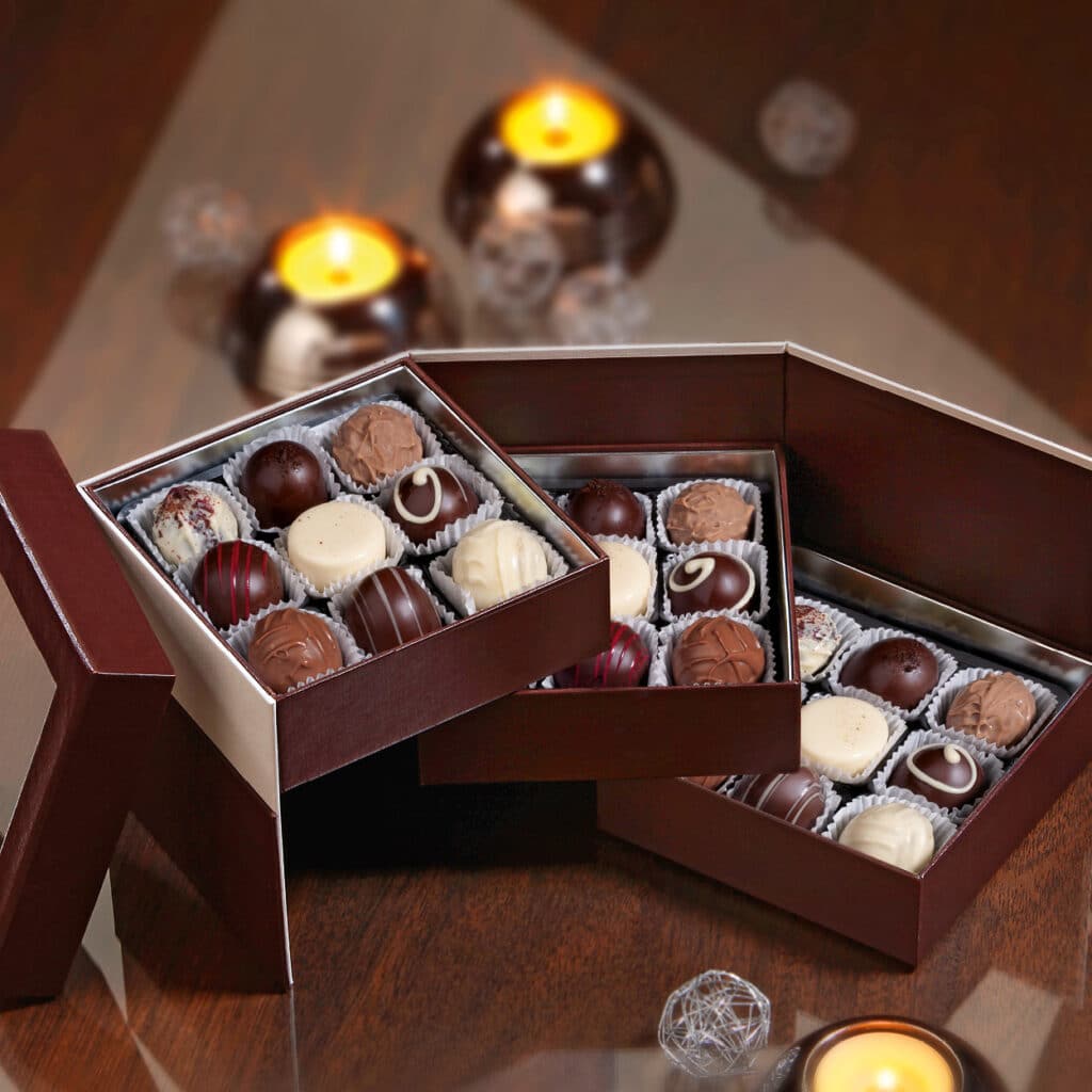 Pralinenauswahl in brauner Geschenkbox, mit weißen, dunklen und roten Schokoladenkugeln, festlich arrangiert.