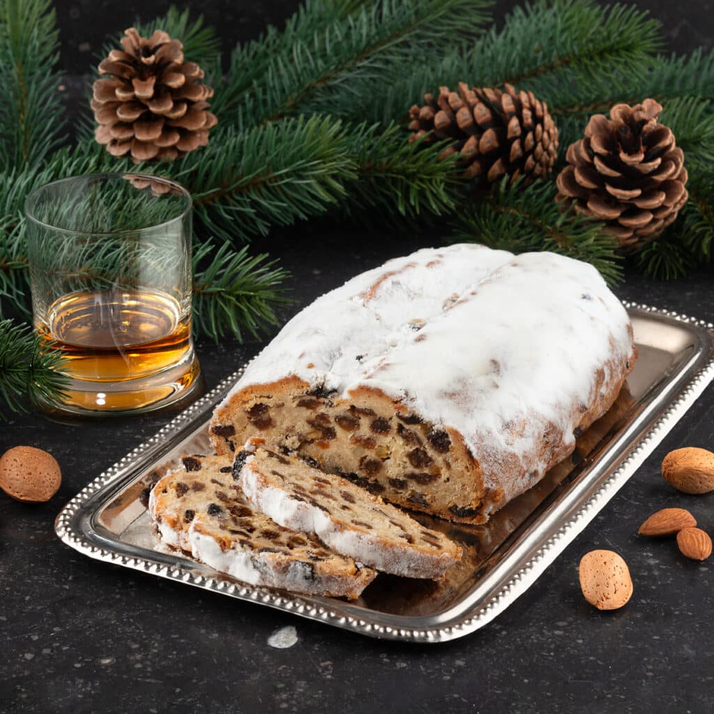 Whiskey-Christstollen mit Puderzucker, Mandeln und Rosinen auf Silbertablett, dekoriert mit Tannenzweigen und Zapfen