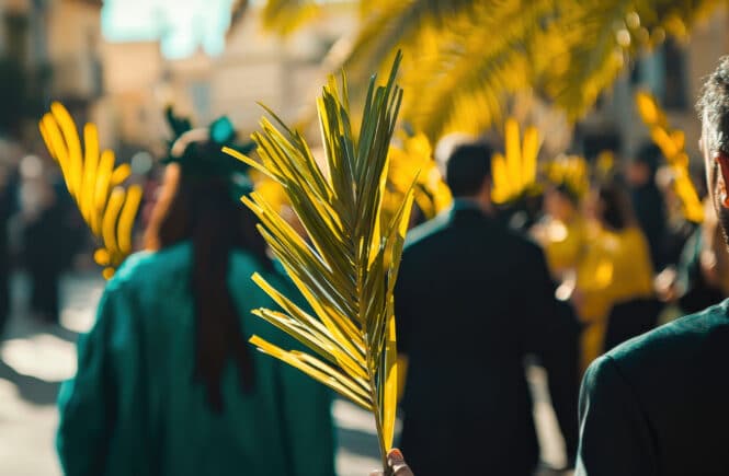 Menschenmenge im Freien, eine Person hält einen grünen Palmzweig, weitere Palmblätter im Hintergrund